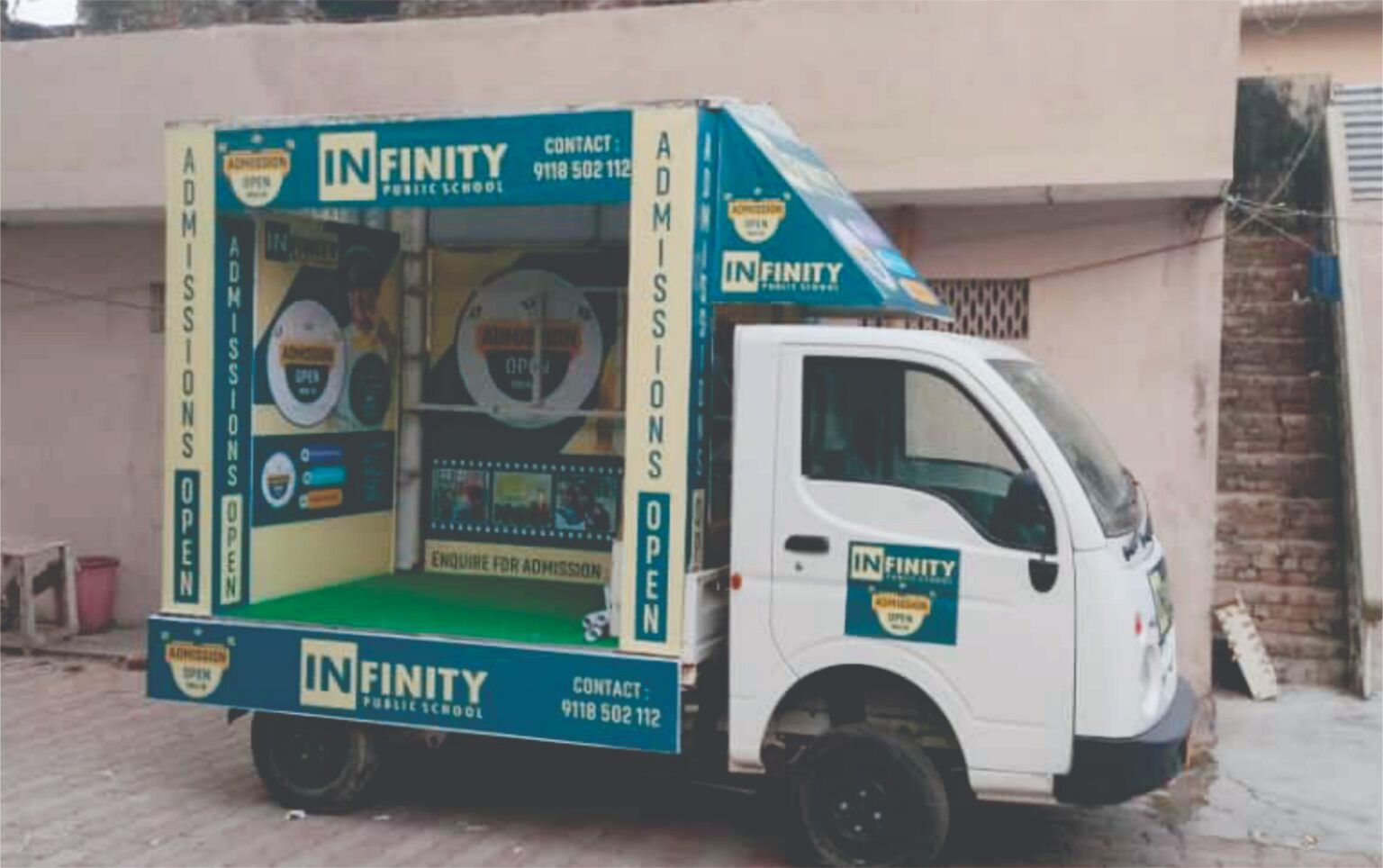 A white color promotional van in Lucknow wrapped with sky blue color flex stand in front of a house